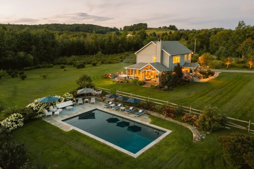 Aerial view of a modern farmhouse with a pool and landscaped yard at golden hour