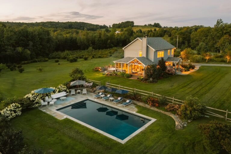 Aerial view of a modern farmhouse with a pool and landscaped yard at golden hour