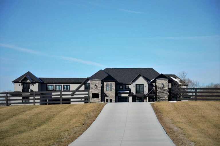 Dark modern home with stone accents and a long concrete driveway